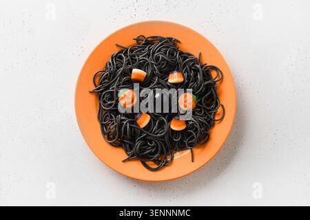 Halloween Alternative kreative italienische schwarze Pasta Tintenfisch Tinte mit lustigen Dekor in orange Platte auf weißem Hintergrund. Blick von oben. Stockfoto
