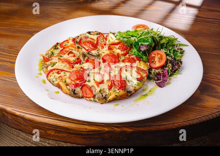 Frittata-Omelett mit Kirschtomaten und frischem Salat, serviert auf einem weißen Teller in einem Café. Die Szene spielt bei Tageslicht in einem Café. Stockfoto