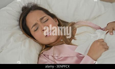Frau mit rosafarbenem Schlafanzug, die Taschentuch an der Nase hält, Hand am Bauch, im Studio auf dem Bett liegend; Krankheit Müdigkeit Unwohlsein. Stockfoto