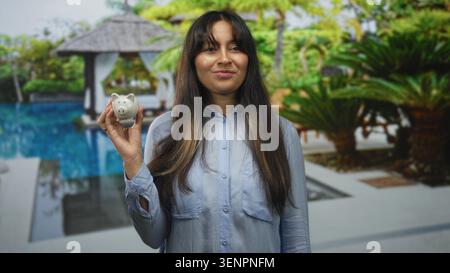 Frau, die eine kleine Keramikbank am Pool hält, die Augen geschlossen und ein leichtes Lächeln; Sparsamkeit. Stockfoto