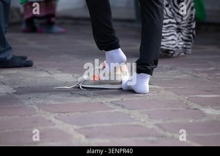 BANGKOK, THAILAND - 23. MAI 2026: Mann, der beige Schuhe auszieht, während er auf einem Steinhof steht Stockfoto