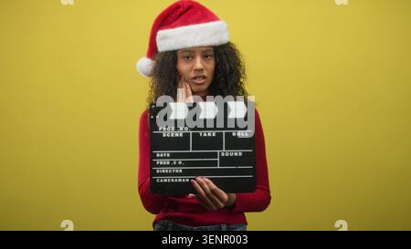 Frau mit Klapptafel und berührender Wange im Studio mit weihnachtsmütze und rotem Pullover; Urlaubsbeschwerden. Stockfoto