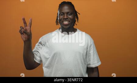 Junger afroamerikanischer Mann in weißem T-Shirt mit doppelten Friedenszeichen mit beiden Händen im Studio mit orangefarbenem Hintergrund; Glück Frieden Positivität. Stockfoto