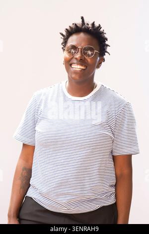 Das Autorenporträt von Julie Nxadi steht draußen, während sie eine Sonnenbrille und ein gestreiftes Hemd trägt. Sie stellt sich selbstbewusst ein lächelndes Posen ein. Stockfoto