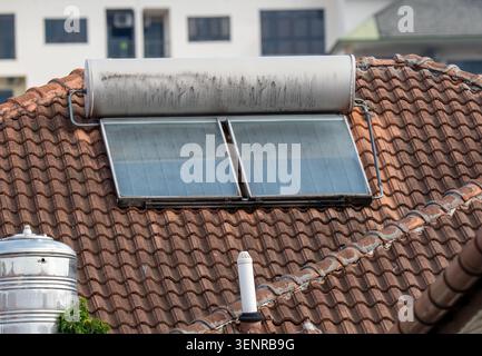 Dachblick auf eine Solaranlage mit Kollektorpaneelen und Speichertank, die auf einem verwitterten Dach aus braunem Lehm installiert sind. Stockfoto
