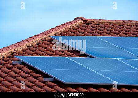 Detaillierte architektonische Aufnahme von zeitgenössischen Photovoltaik-Solarmodulen, die auf einem Wohndach aus orangen Terrakotta-Tonziegeln installiert sind. Stockfoto