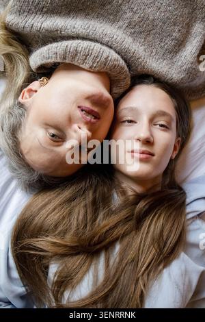 Zärtliches Porträt von Mutter und Teenager-Tochter, die auf gemütlichem Bett in der Berghütte liegen. Warmer, authentischer Familienzusammenhalt mit weichem, natürlichem li Stockfoto