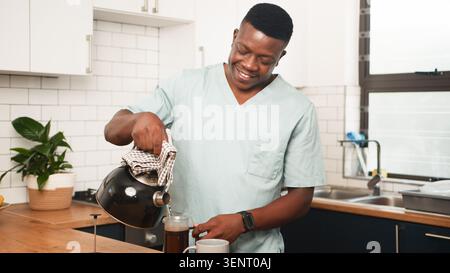 Lächelnder Arzt, Der Kaffee In Der Modernen Küche In Der Morgenpause Gießt Stockfoto