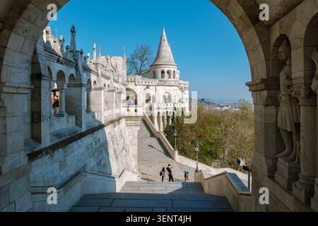 Budapest, Ungarn, 10. April 2026. Besucher bewundern die atemberaubende Architektur der Burg Buda, während sie die große Treppe hinuntergehen. Die Sonne beleuchtet die komplizierten Details vor einem klaren blauen Himmel. Stockfoto