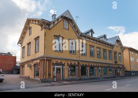 LOVIISA, FINNLAND - 15. AUGUST 2025: Traditionelles Geschäftsgebäude aus gelbem Ocker mit verziertem Giebeldach an der Ecke in der alten europäischen nordischen Stadt. Stockfoto