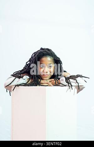 Porträt der attraktiven Yoiung-Schriftstellerin Tomi Adeyemi vor weißem Hintergrund. Sie hat lange Dreadlocks und trägt ein weißes Top. Stockfoto