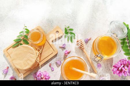 Honiggläser mit Löffeln, frische Akazienblüten und Blätter auf hellem Hintergrund Stockfoto