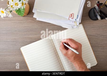 Draufsicht einer Handschrift in einem Notizbuch neben gestapelten Dokumenten und Büromaterialien, die Planung, Notizen, Organisation und Produktivität veranschaulicht Stockfoto