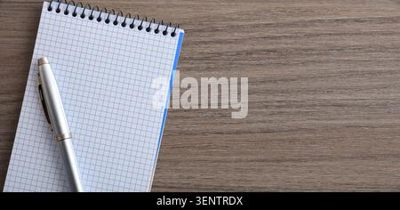 Minimalistischer Draufsicht eines leeren Spiralnotizbuches und Silberstifts auf einem Holztisch, der Platz zum Kopieren von Notizen, Planungen oder kreativen Schreiben bietet. Stockfoto