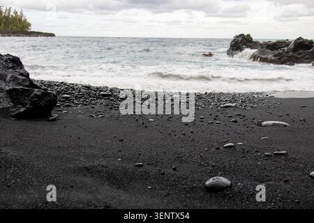 Flacher Blick auf glatte schwarze Lavasteine und weiße Ozeanwellen auf Big Island Hawaii Stockfoto