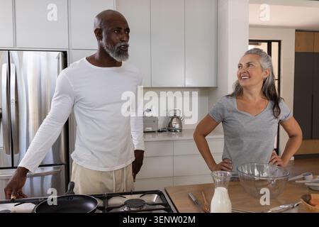 Diverse Pärchen stehen in der modernen Küche, Mann hält eine Pfanne und lächelt eine Frau Stockfoto