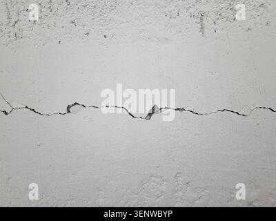 Verdrehter langer horizontaler Riss an einer lackierten grauen Wand. Zerstörung nach dem Erdbeben. Gerissene Betonoberfläche. Reparatur, Bau von Gebäuden, Stockfoto