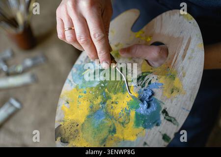 Nahaufnahme einer Holzpalette mit bunten Farben in Künstlerhänden. Malprozess, Kreativität, Kunst, Inspiration und künstlerisches Arbeitskonzept Stockfoto