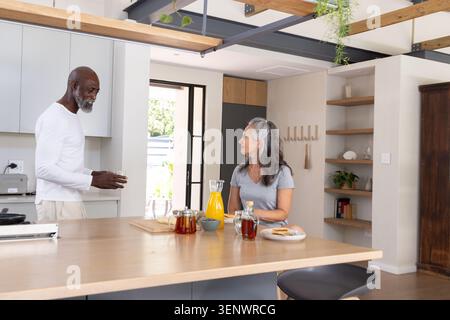 Diverse Seniorenpaare unterhalten sich auf der Kücheninsel mit einem Glaskrug mit Orangensaft und Gebäck Stockfoto