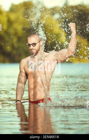 Muskeltätowierter Mann, der im Sommer im Wasser des Stadtsees hingerichtet wird Stockfoto