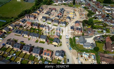 Ein Blick aus der Vogelperspektive zeigt eine neue Wohnsiedlung mit laufendem Bau, umgeben von etablierten Vierteln und einem Sportplatz in Noble Stockfoto