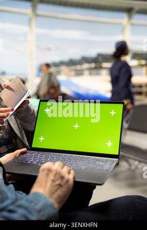Green Screen Mockup auf Laptop, der von älteren Paaren im Wartebereich am Flughafen benutzt wird, Vorbereitung von Reiseplänen und Besichtigungsterminen. Glückliche Senioren, die Abenteuer und Leben nach dem Ruhestand genießen. Stockfoto