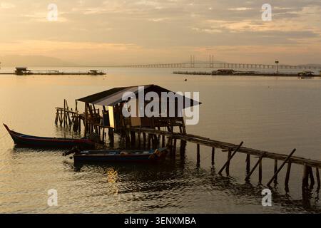 Der hölzerne Steg liegt über ruhigem Wasser, während die Sonne nahe Georgetown auf Penang Island in Malaysia aufgeht Stockfoto