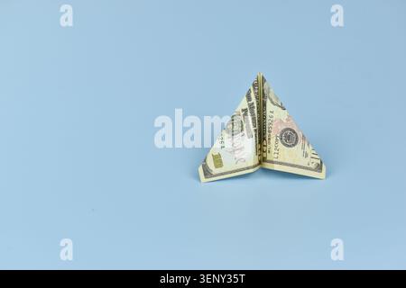 Gefalteter Dollarschein erzeugt eine zarte Schmetterlingsform. Seine Flügel ahmen den Flug nach, als ob sie bereit wären, in die Höhe zu fliegen. Der sanfte blaue Hintergrund verstärkt seine künstlerische Einfachheit Stockfoto