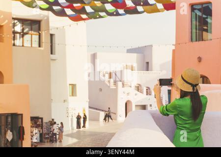 Doha, Katar - 8. januar 2026: Frau, die sich auf einen Balkon stützt und Fotos im Stadtteil Mina in Doha macht, umgeben von bunten Gebäuden und Schatten Stockfoto