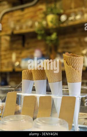 Waffel-Eiskegel sind ordentlich in einem Ausstellungsstand mit leeren braunen Etiketten auf einer Serviertheke gestapelt und warten darauf, mit süßem, gefrorenem Leckerli gefüllt zu werden Stockfoto