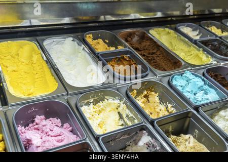 Viele verschiedene Geschmacksrichtungen der Eisfüllung von Edelstahlbehältern in einer gekühlten Vitrine, die eine Vielzahl von Farben und Texturen des Schalters zeigt Stockfoto