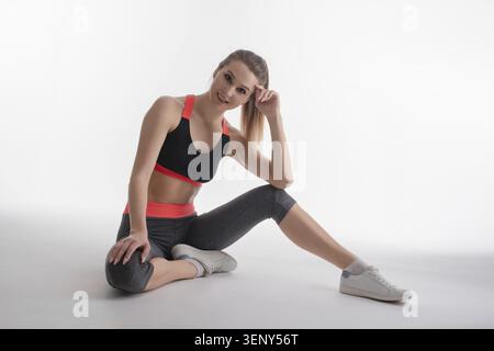 Eine Frau posiert elegant in einem sportlichen Outfit und zeigt Athletik und Anmut in einem professionellen Studio-Setting Stockfoto