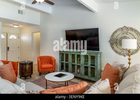 Stilvolles Wohnzimmer mit Stühlen mit leuchtenden orangefarbenen Akzenten, Konsolentisch in rustikalem Petrol, Sofa, Kissen mit Akzenten, Couchtisch und Flachbildfernseher Stockfoto