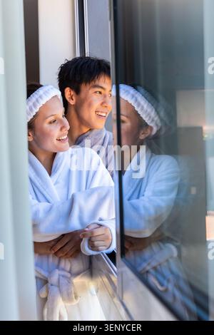 Verschiedene Paare stehen vor der Tür und tragen weiße Bademäntel und Frottee-Stirnband, das sich in Glas spiegelt Stockfoto