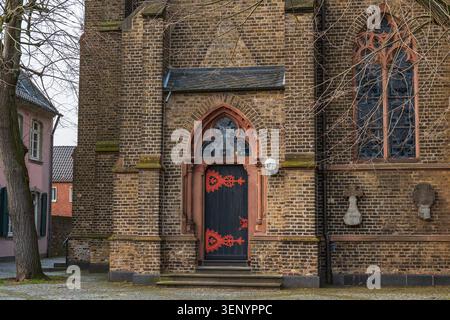 Eingang gotischer Architektur durch die Kirchentür, Fassade der alten mittelalterlichen Backsteinkathedrale mit bogenförmigem Holzeingang, roten Metallornamenten, Buntglasfenster Stockfoto