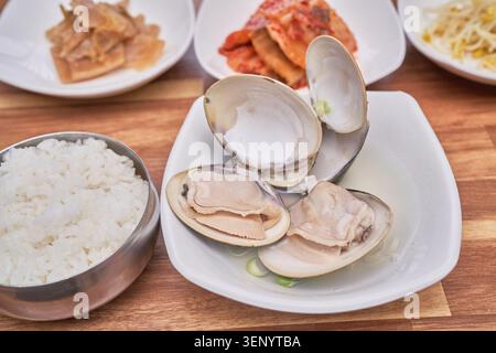 Traditionelle koreanische Gerichte umfassen frische große Biventilen, die in einer klaren Brühe gekocht werden, kombiniert mit gedämpftem weißem Reis und verschiedenen Beilagen wie scharfen Kimchi Stockfoto