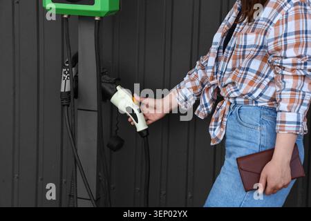 Frauen halten den Stecker des Ladekabels für Elektrofahrzeuge für nachhaltigen Transport und umweltfreundliche Energie in der Zukunft. Diese Aktion stellt den Wandel dar Stockfoto