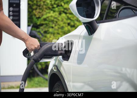Das Ladegerät mit der Hand an ein Elektroauto anschließen. Konzentration auf moderne Elektrofahrzeuge. Sauberes Aufladen leise Außenstation öffentlich. Einfache nachhaltige Trans Stockfoto