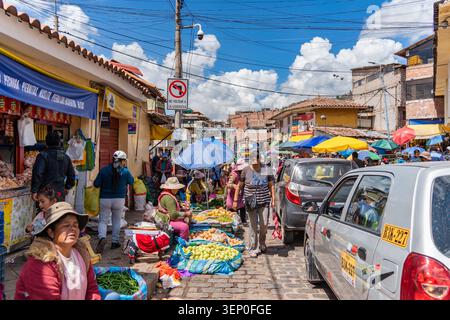 Cusco, Peru - 23. März 2025: Lokale Händler sitzen auf der Kopfsteinpflasterstraße und zeigen bunte Haufen frisches Obst und Gemüse unter Sonnenschirmen. Stockfoto