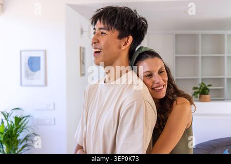 Diverse Paare lachen und umarmen im Wohnzimmer zu Hause mit Regalen, Pflanzen, Stirnband Stockfoto