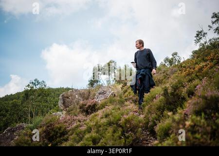 Ein Mann, der einen Pfad bergauf geht, ein Telefon hält und die Aussicht ansieht Stockfoto