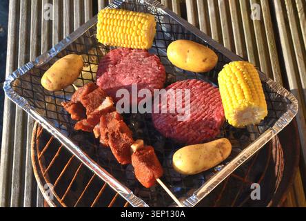 Rohe Rindfleischburger, Mais auf dem Kolben, Kartoffeln und Fleischspieße, die auf einem Einweg-Grilltablett gekocht werden, Hochwinkelansicht Stockfoto