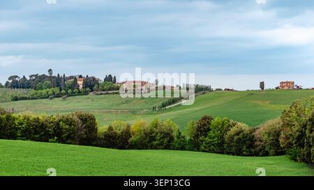 Sanfte grüne Hügel und ferne Villen unter bewölktem Himmel in der Toskana, Italien. Stockfoto