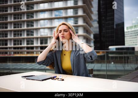 Geschäftsfrau mit Kopfschmerzen, die unter Stress und Burnout im Büro leidet Stockfoto