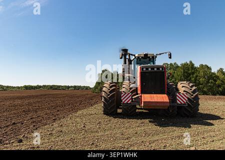 Großer landwirtschaftlicher Traktor auf bewirtschaftetem Feld unter blauem Himmel Stockfoto