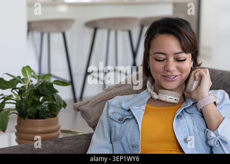 Afroamerikanerin sitzt zu Hause auf dem Sofa in einer Jeansjacke mit Kopfhörern, Kopierraum Stockfoto