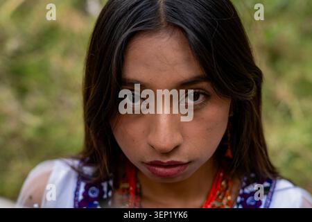 Junge einheimische Frau mit dunklem Haar und traditioneller Kleidung, die den Zuschauer mit einem intensiven und ernsten Blick direkt ansieht und dabei das Erbe und die Tradition repräsentiert Stockfoto