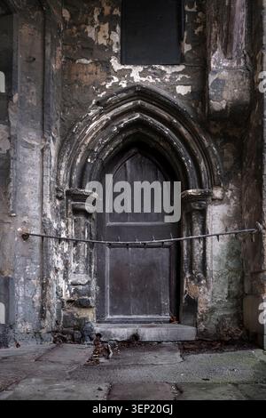 Oxford, Oxfordshire: Verwitterter gotischer Steineingang in einer alten architektonischen Fassade mit spitzem Bogen, dunkler Holztür und abblätternder Oberfläche Stockfoto