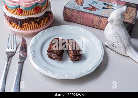 Schokoladen-Sandwich-Kuchenhälften auf weißem Teller im Stillleben-Arrangement. Weiches, diffuses Licht hebt Texturen hervor. Süßwarenkonzept für Stockfoto
