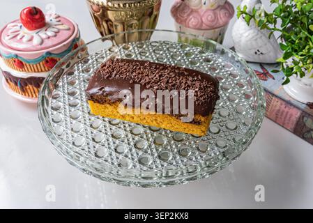 Nahaufnahme von Karottenkuchen auf Glasplatte, isoliert auf weiß. Kuchen hat helle Farben, glatte Texturen und Deckenbeleuchtung. Partykonzept, cate Stockfoto